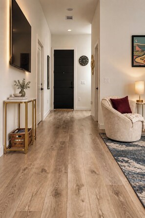 A hallway with a wooden floor, a black door, a wall clock, a television, and a sofa with a throw blanket. - Regent Sol - Scandinavian Luxury - Central Austin (Austin)