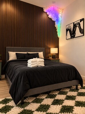 A modern bedroom with a large bed, a wall-mounted lamp, and a checkered rug. - Regent Sol - Scandinavian Luxury - Central Austin (Austin)