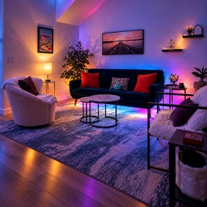 A modern living room with a sofa, armchair, and coffee table, a large plant, and artwork on the walls. - Regent Sol - Scandinavian Luxury - Central Austin (Austin)