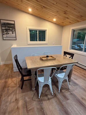 A dining area with a wooden table, white chairs, and a window. - Tree top views, 1 mile to Mt Snow, spacious getaway , family & pet friendly (Dover)
