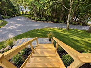 Eine Holztreppe führt zu einer grünen Fläche mit einem Kiesweg und Bäumen im Hintergrund.