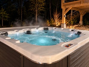 Ein Whirlpool mit einer Holzterrasse und einer Steinwand im Hintergrund.