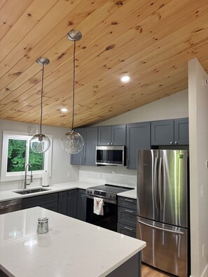A modern kitchen with wooden ceiling beams, stainless steel appliances, and a large island. - Tree top views, 1 mile to Mt Snow, spacious getaway , family & pet friendly (Dover)