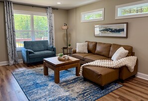 Ein Wohnzimmer mit einem braunen Ledersofa, einem blauen Sessel, einem Holztisch und einem blau-weißen Teppich.