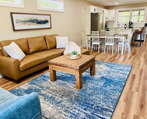 Een woonkamer met een bruine leren bank, een houten salontafel en een blauw vloerkleed met dessin.