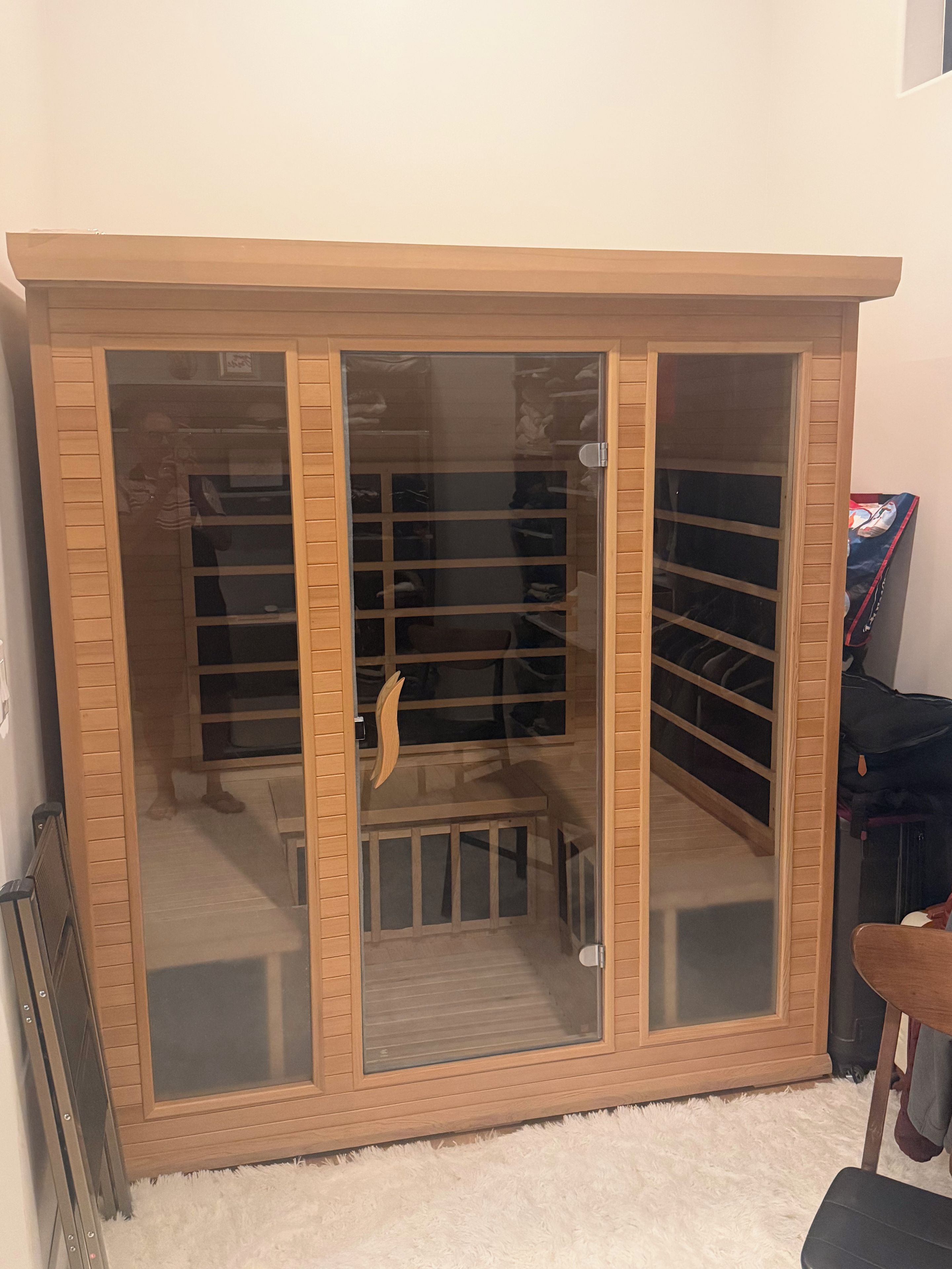 Una habitación con un armario grande de madera con puertas de cristal, una alfombra blanca y mullida, y un pequeño banco de madera.