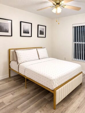 Un dormitori amb un llit, un ventilador de sostre i tres quadres a la paret.