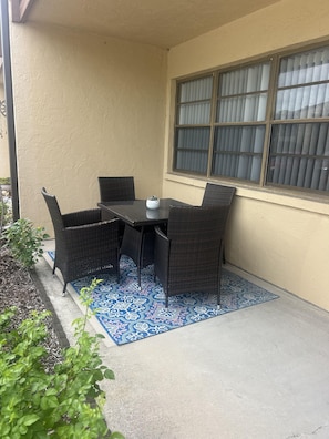 An outdoor patio with a table and chairs, a window with blinds, and a blue patterned rug. - Relax & Unwind in Englewood at Quails Run, over 55 community in Englewood. (Englewood)