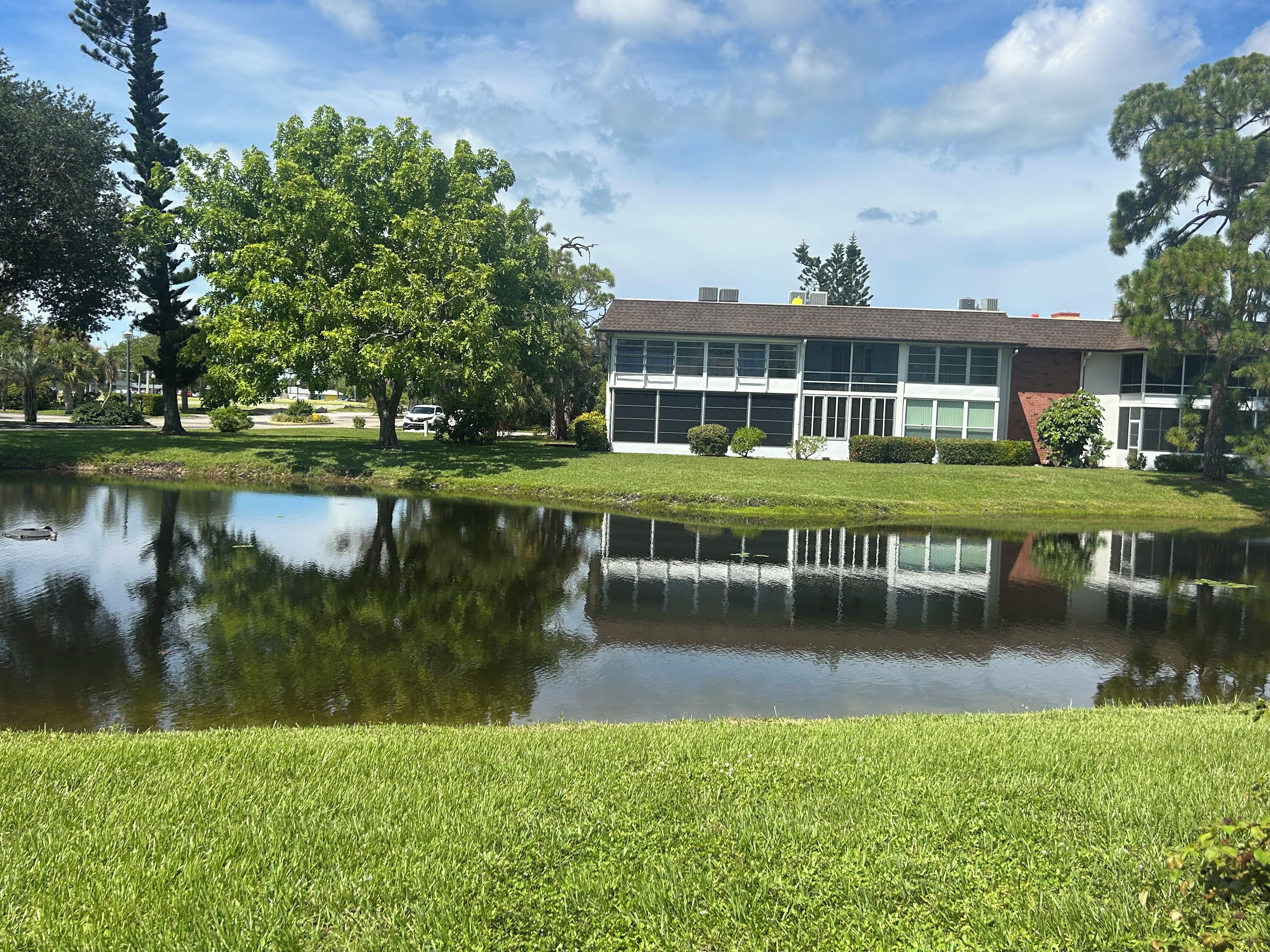 A building with a reflective pond in front, surrounded by grass and trees.