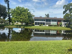 A building with a reflective pond in front, surrounded by grass and trees. - Relax & Unwind in Englewood at Quails Run, over 55 community in Englewood. (Englewood)