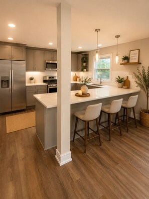 A modern kitchen with stainless steel appliances, a large island with bar stools, and a view of the outdoors. - Furnished Studio | 2 Full Beds | Short & Mid-Stay (Crystal Lake)