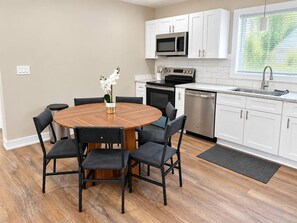 A modern kitchen with white cabinets, a stainless steel sink, and a round wooden table with chairs. - Furnished Studio | 2 Full Beds | Short & Mid-Stay (Crystal Lake)