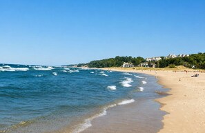 Ein Strand mit Wellen, einem Sandufer und Häusern im Hintergrund.