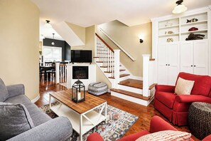 Ein Wohnzimmer mit Kamin, einem roten Sofa, einem grauen Sofa, einem Holztisch und einer Treppe.