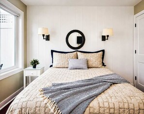 Ein Schlafzimmer mit einem Bett, Nachttischlampen, einem Spiegel und einem Fenster.
