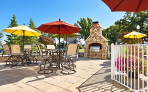 Un patio al aire libre con una parrilla de piedra, rodeado de sillas y mesas bajo sombrillas.