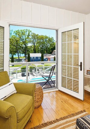 A room with a sliding glass door leading to a balcony with a pool and outdoor furniture. - The Newport | Pool • Hot Tub • Lake • Free Golf (Holland)