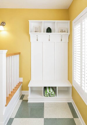 A hallway with a white bench, a wall-mounted shelf with decorative items, and a window with shutters. - The Newport | Pool • Hot Tub • Lake • Free Golf (Holland)