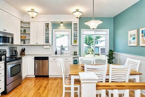A modern kitchen with white cabinetry, stainless steel appliances, and a wooden dining table with white chairs. - The Newport | Pool • Hot Tub • Lake • Free Golf (Holland)