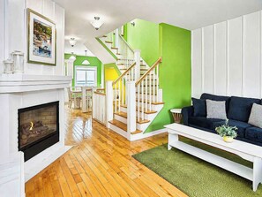 Un salon avec une cheminée, un escalier aux murs peints en vert et un canapé de couleur foncée.