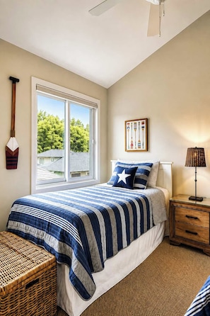 A bedroom with a large window, a bed with a blue and white striped bedspread, a wooden nightstand, a wicker basket, and a wall-mounted lamp. - The Charleston | Pool • Hot Tub • Lake • Free Golf (Holland)