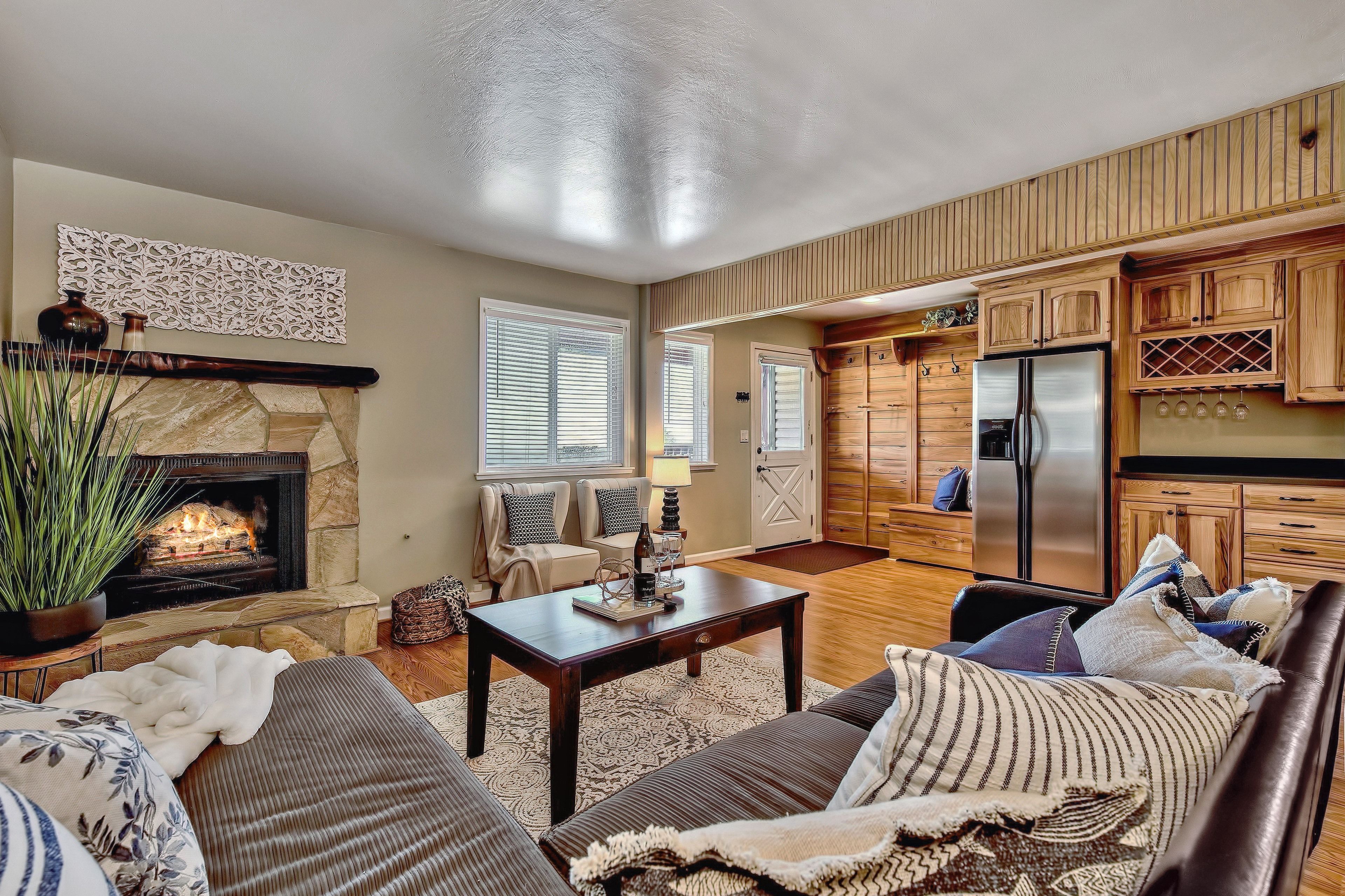 A living room with a fireplace, seating area, and kitchen with wooden cabinets.