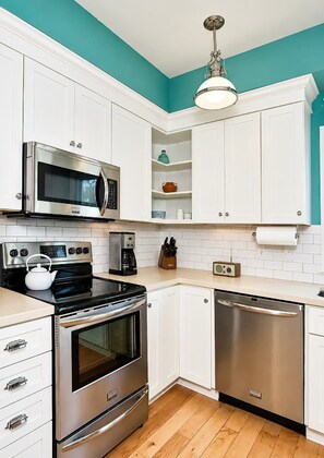 A modern kitchen with white cabinets, stainless steel appliances, a teal accent wall, and a wooden floor. - The Marblehead | Pool • Hot Tub • Lake • Free Golf (Holland)