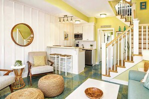 A spacious living area with a sofa, armchair, and a dining table with stools. A kitchen with a microwave and a refrigerator is visible in the background. - The Marblehead | Pool • Hot Tub • Lake • Free Golf (Holland)