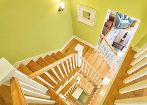 Eine Treppe führt zu einem Wohnbereich mit grüner Wand, Holzboden und einem gerahmten Spiegel.