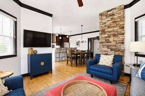 Ein modernes Wohnzimmer mit einem Flachbildfernseher, blauen Sofas, einer Wand aus Naturstein und einem Essbereich mit einer Kronleuchter.