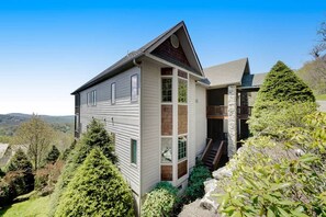 Ein zweistöckiges Haus mit Natursteinfassade, einer Holzterrasse und Blick auf die umliegende Landschaft.
