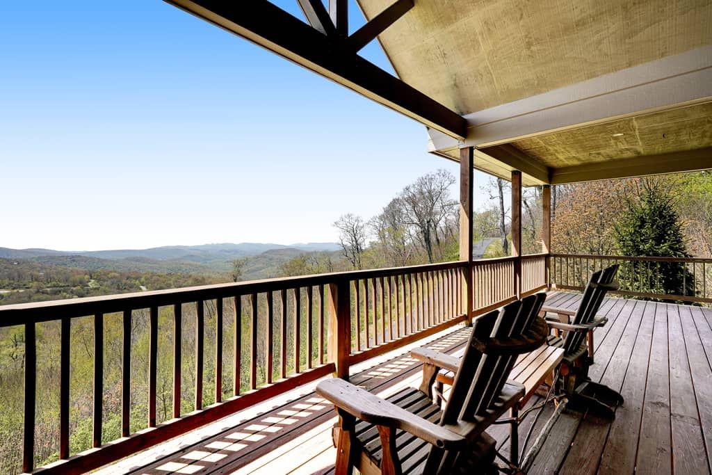 A wooden deck with a view of the mountains, wooden chairs, and a covered area.
