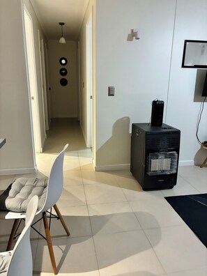 Ein Zimmer mit einem Sessel, einem Heizstrahler, einem an der Wand befestigten Fernseher und einer Tür zu einem weiteren Raum.