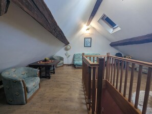 Une pièce de style loft avec un plafond en bois, une table à manger agrémentée d’un centre de table floral, deux canapés à motifs et une rambarde en bois.