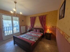 Une chambre à coucher comprenant un lit, une table de chevet, une lampe, une fenêtre avec des rideaux et un lustre.
