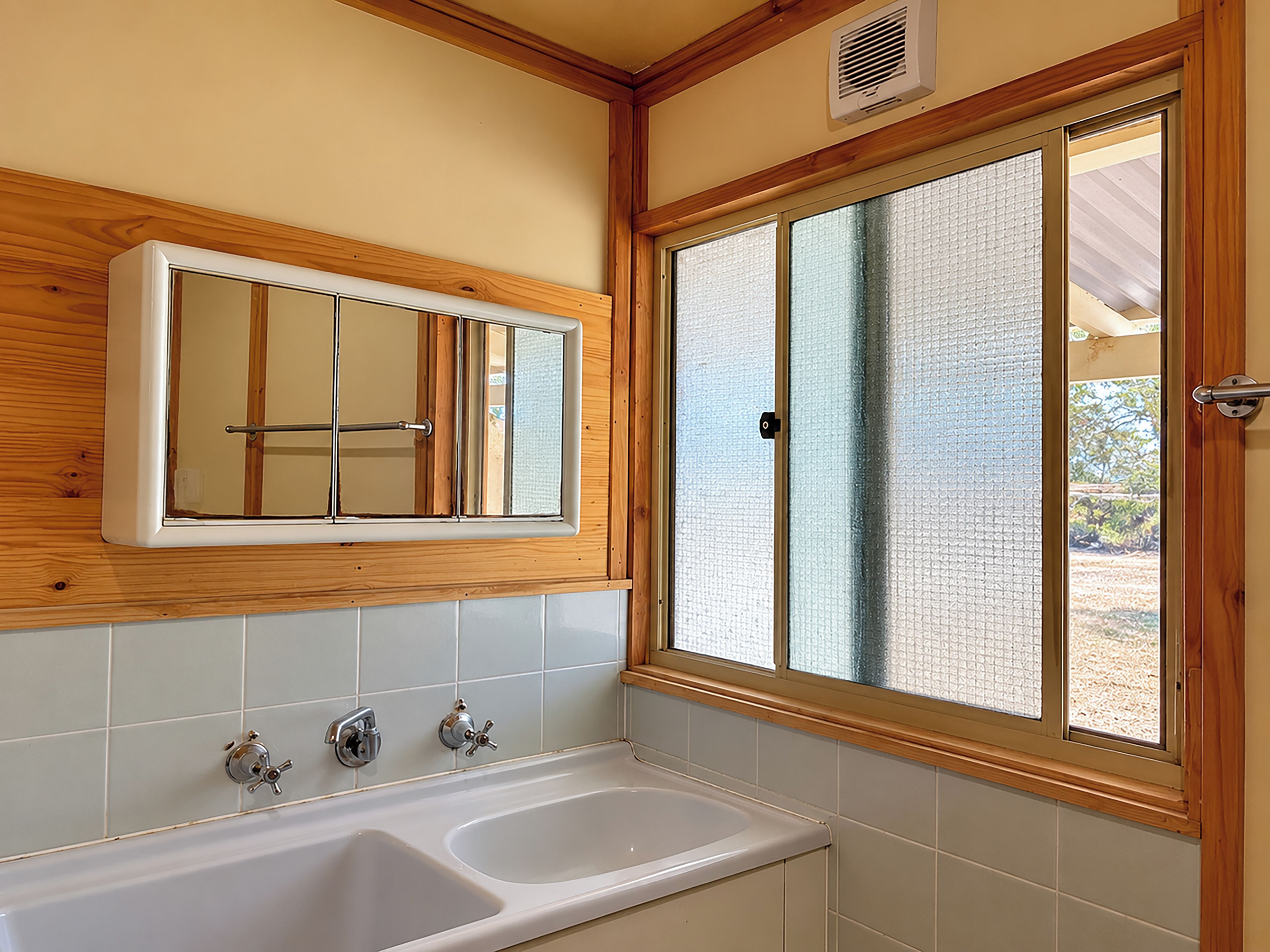 A bathroom with a double sink, wooden paneling, a mirror, and a window with frosted glass.