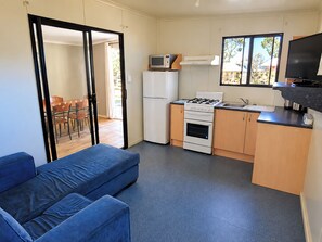 A compact kitchen with a gas stove, microwave, and refrigerator. There's a blue sofa and a dining area visible through an open door.