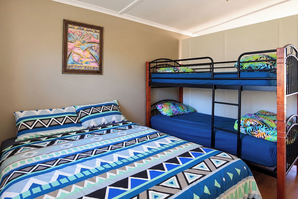 A bunk bed with a patterned bedspread, a framed artwork on the wall, and a wooden headboard.