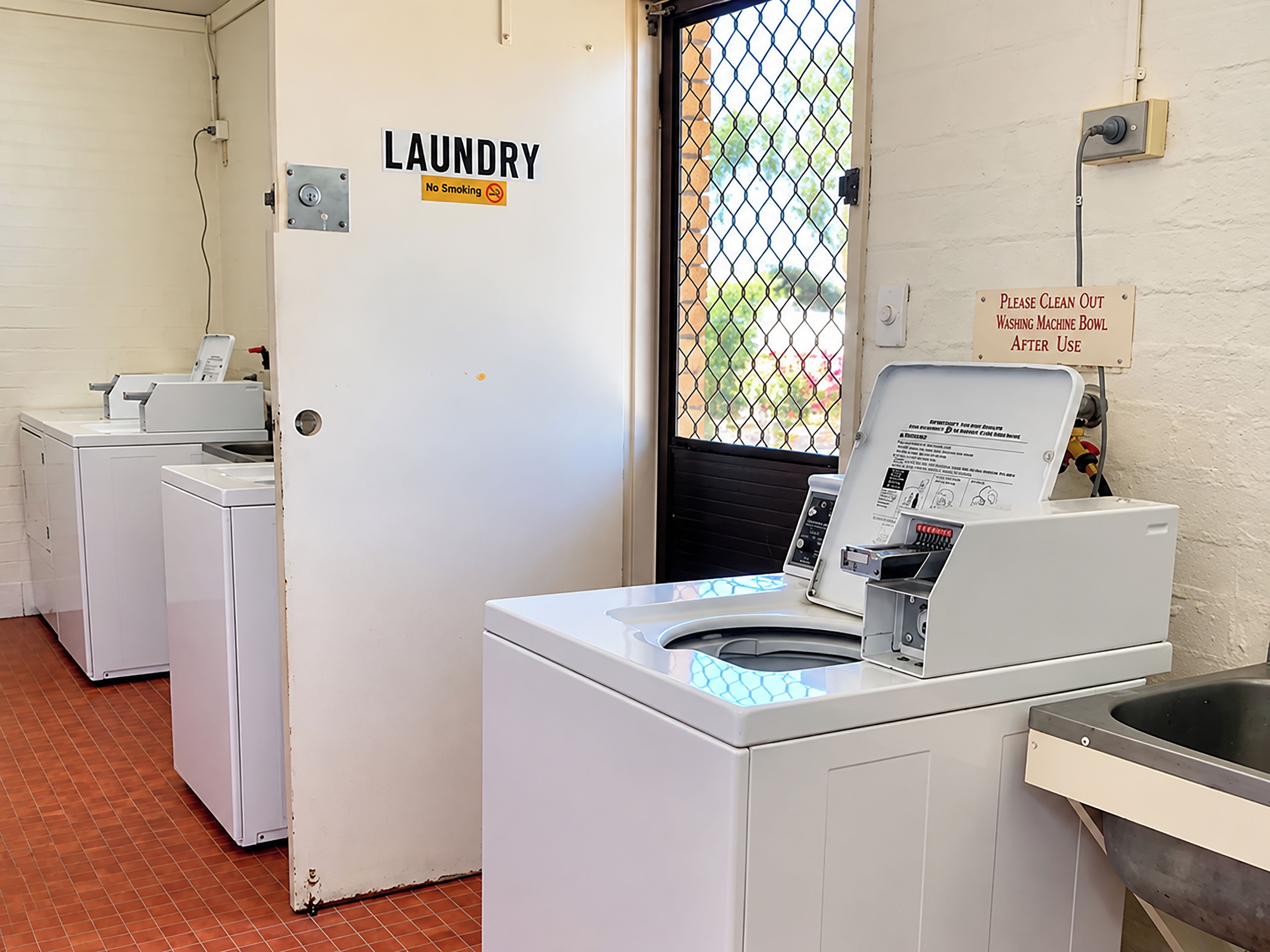 Ein Waschraum mit einer Tür mit der Aufschrift 'LAUNDRY' und einem Schild, das dazu auffordert, die Waschmaschine nach Gebrauch auszuwischen.