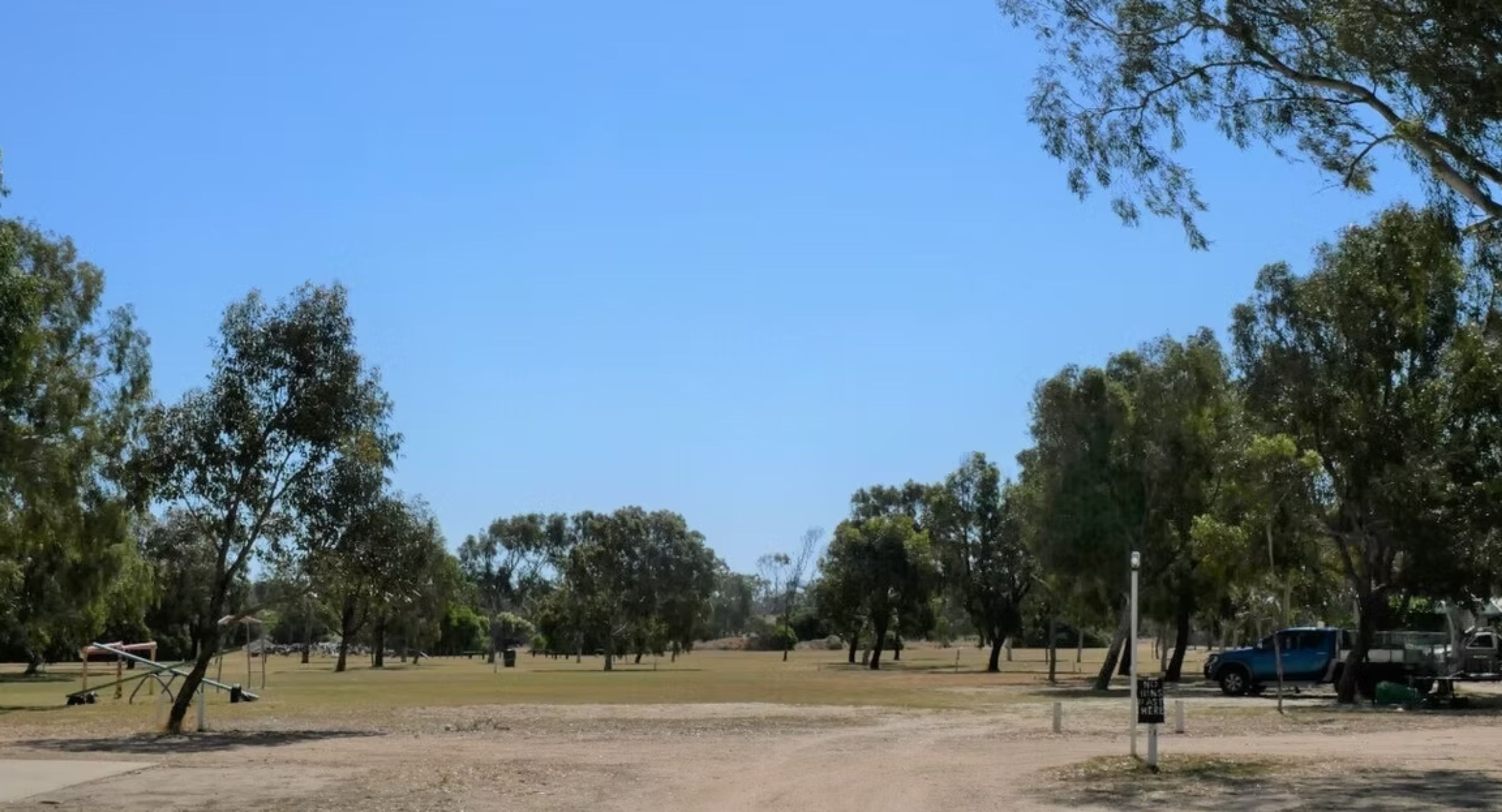 A park with trees, a playground, and a dirt path.