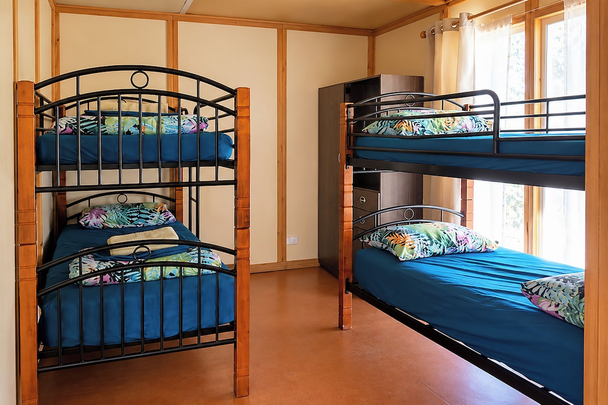 A bunk bed room with a wooden ceiling and a window with curtains.
