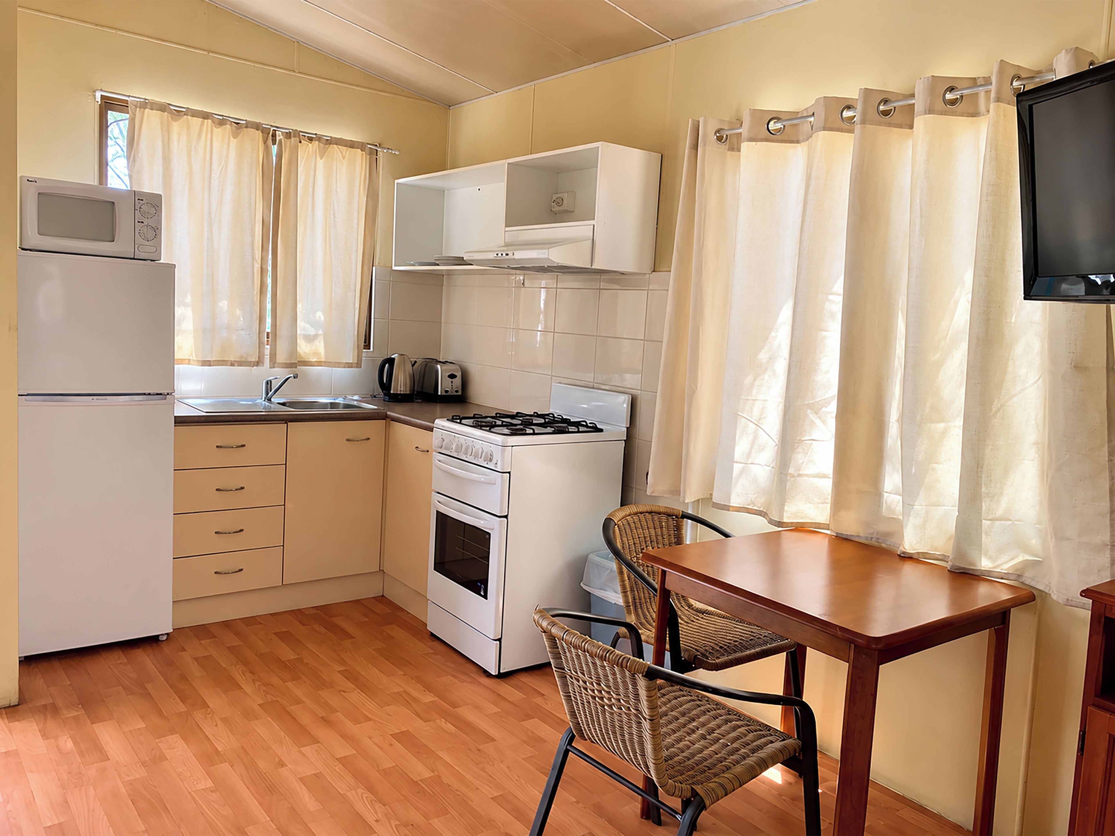A compact kitchen with a refrigerator, microwave, toaster, stove, and a dining area with a table and chairs.