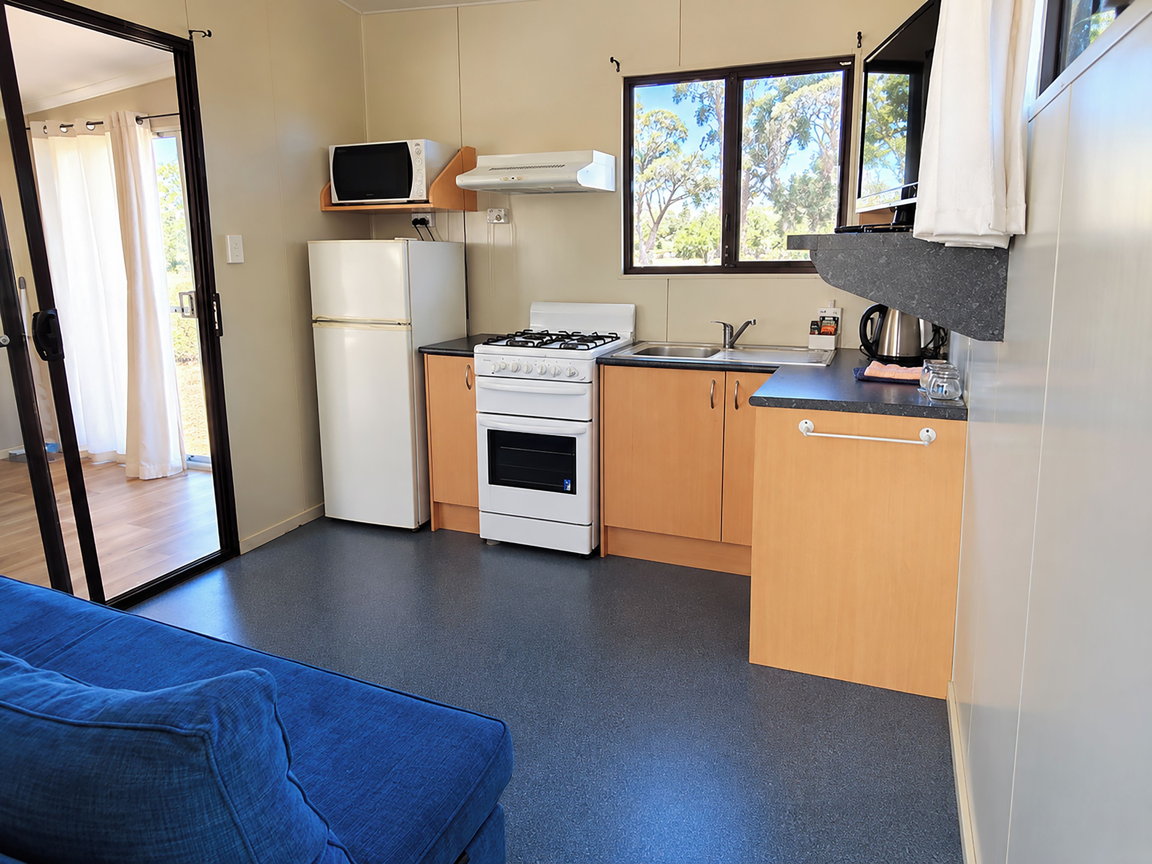 A compact kitchen with a refrigerator, stove, microwave, and a window with a view of trees.