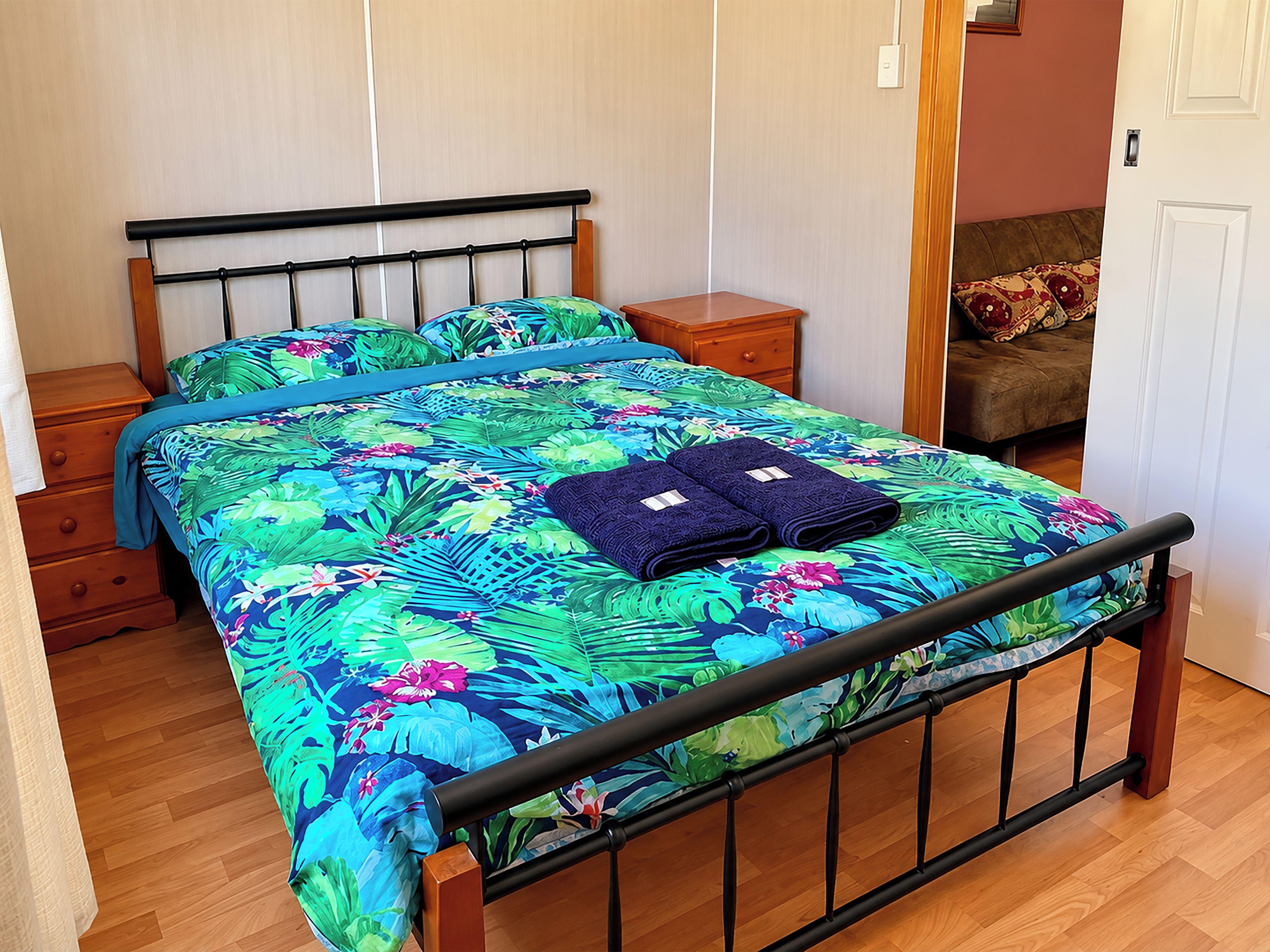 A bed with a floral bedspread, two folded towels, a wooden nightstand, and a wooden dresser.