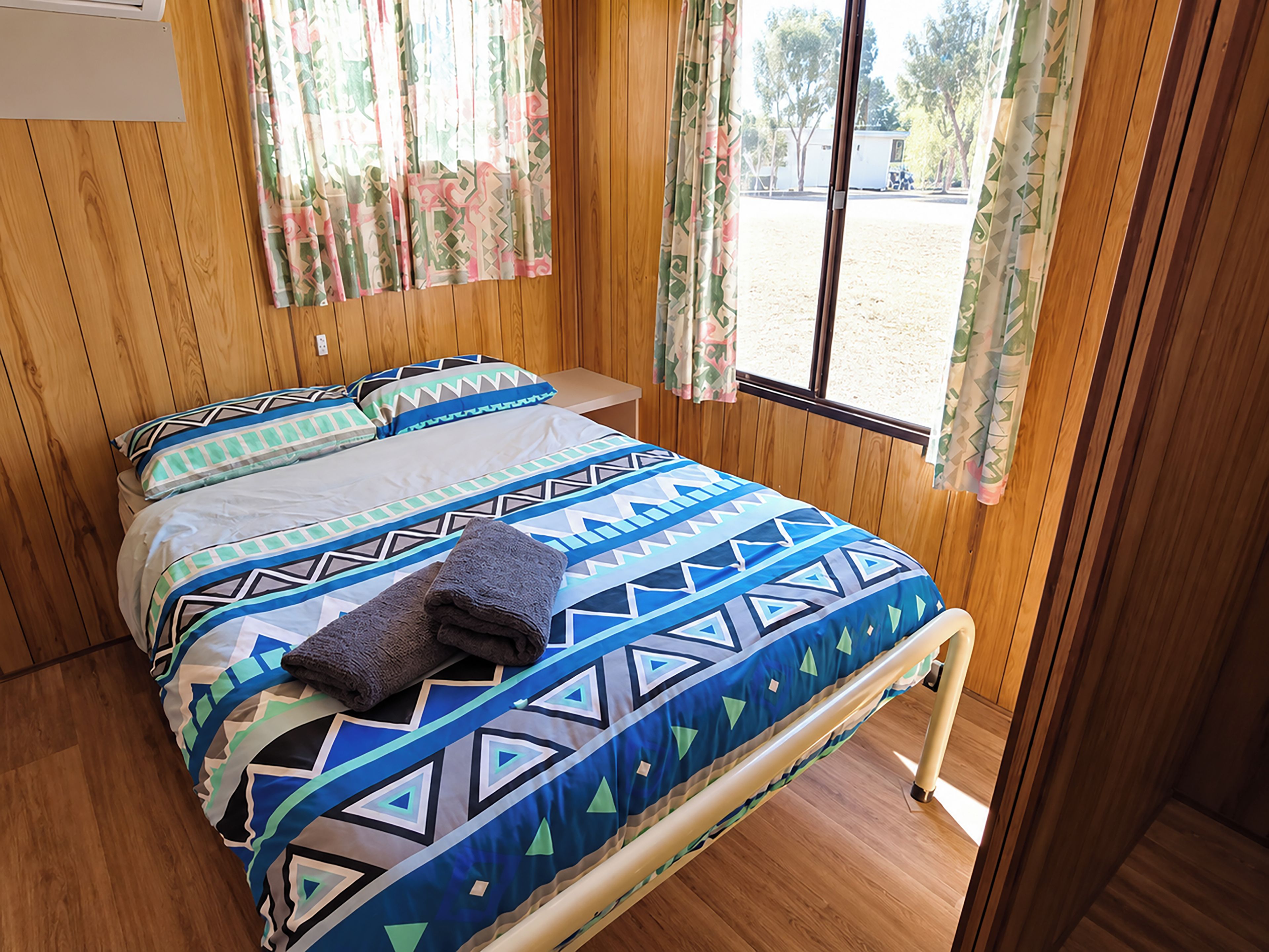 A room with a bed, wooden walls, a window with curtains, and a view of the outside.