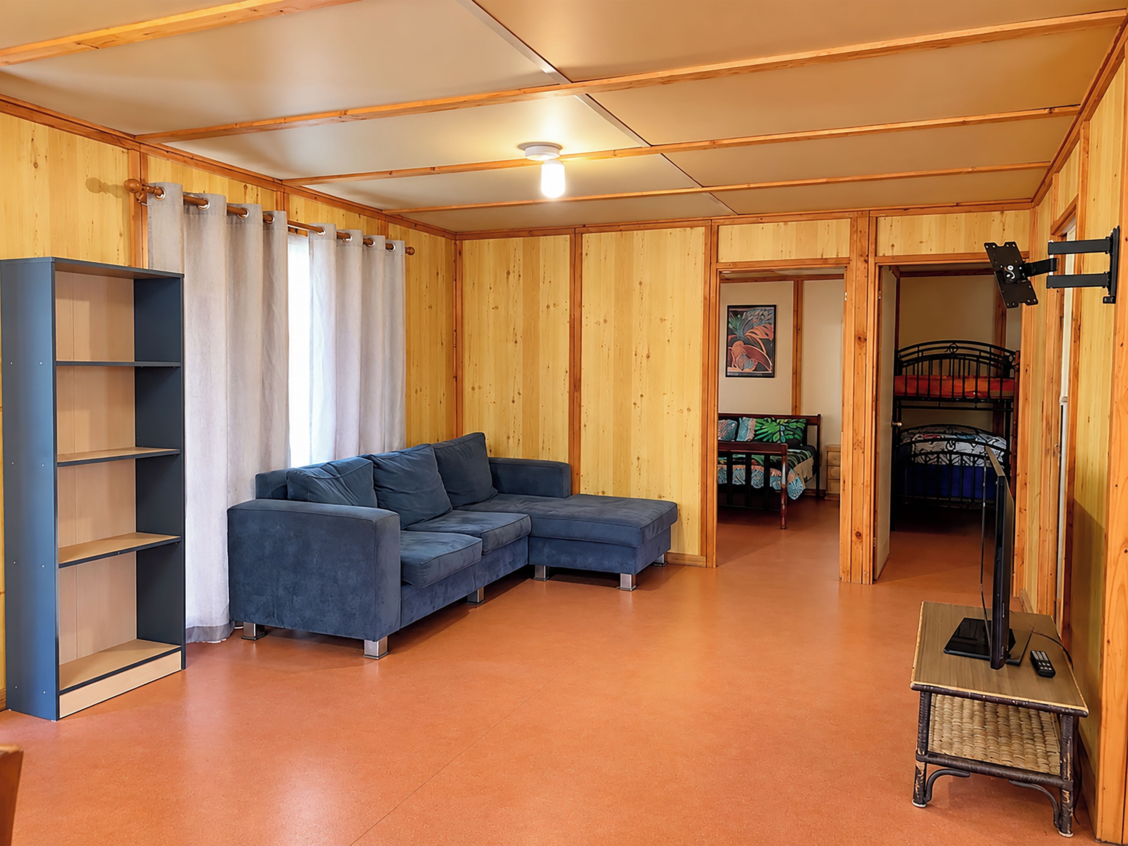 A room with a sectional sofa, a small table with a computer, and a bunk bed in the background.
