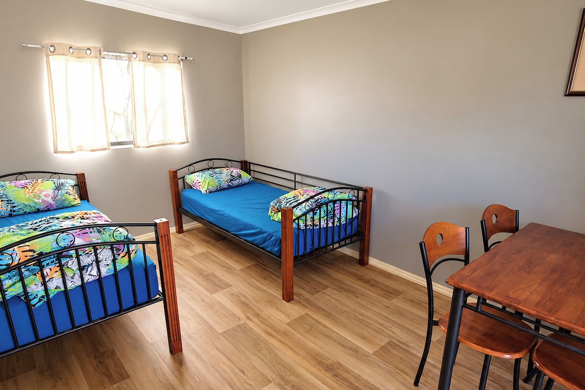A room with two single beds, a wooden dining table, and a window with curtains.