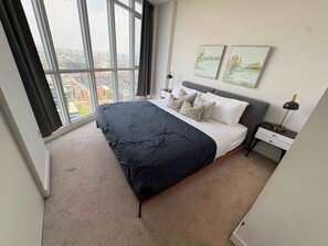 A modern bedroom with a large bed, a nightstand, a lamp, and two wall-mounted paintings. - Modern Core 1BR Oasis Walk to Rogers Centre! (Toronto)
