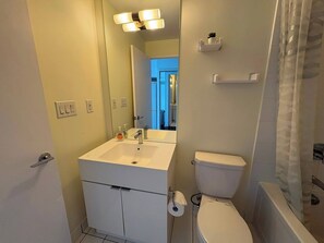 A bathroom with a white sink, toilet, and a mirror. There is a towel rack above the toilet and a shower curtain on the right. - Modern Core 1BR Oasis Walk to Rogers Centre! (Toronto)