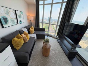A modern living room with a large window, a sofa, a coffee table, and a flat-screen TV. - Modern Core 1BR Oasis Walk to Rogers Centre! (Toronto)